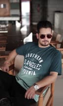 Man wearing a green t-shirt with text, sitting in a casual setting.