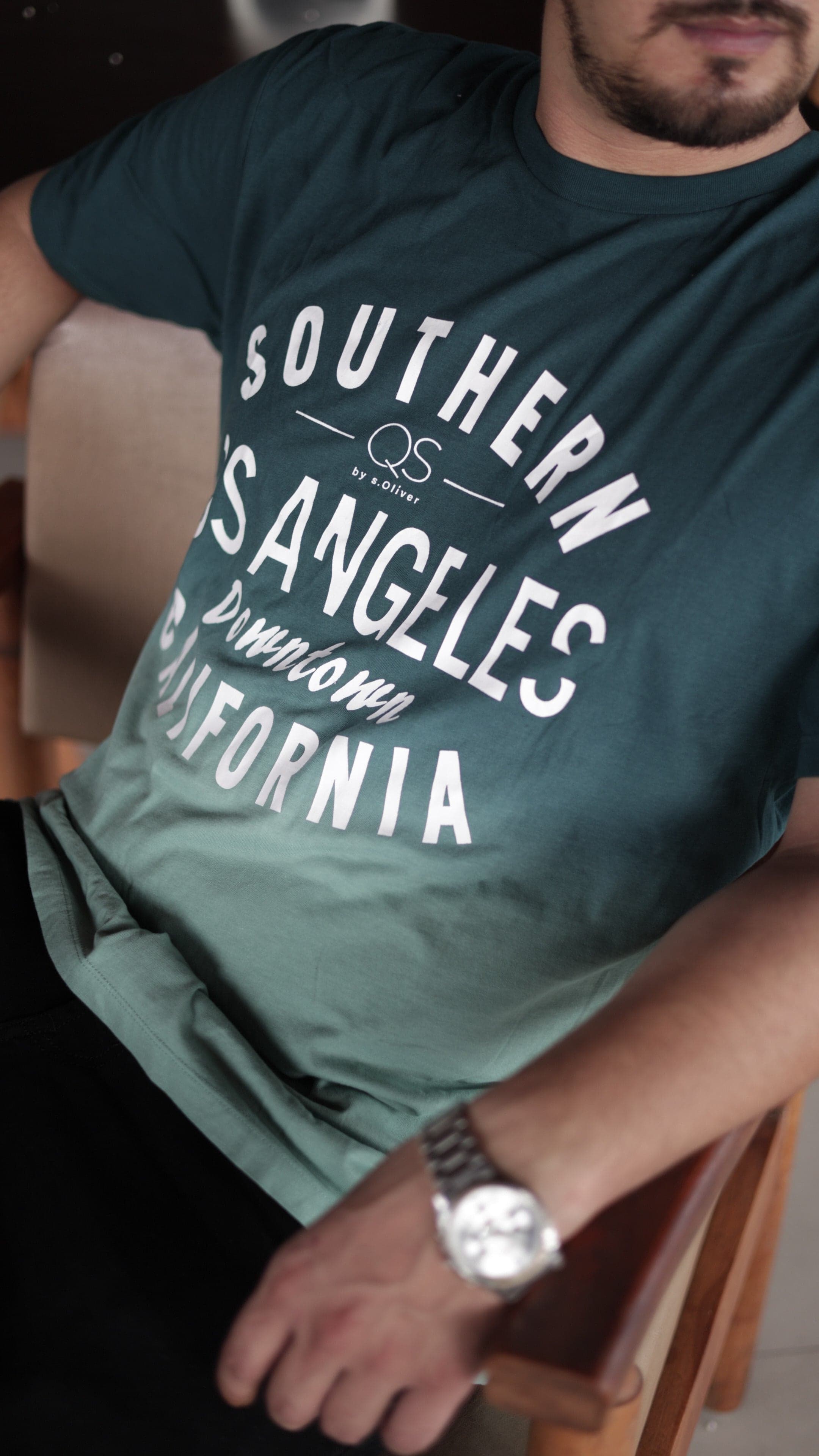 Person wearing a green t-shirt with 'Southern California' text, sitting on a chair.