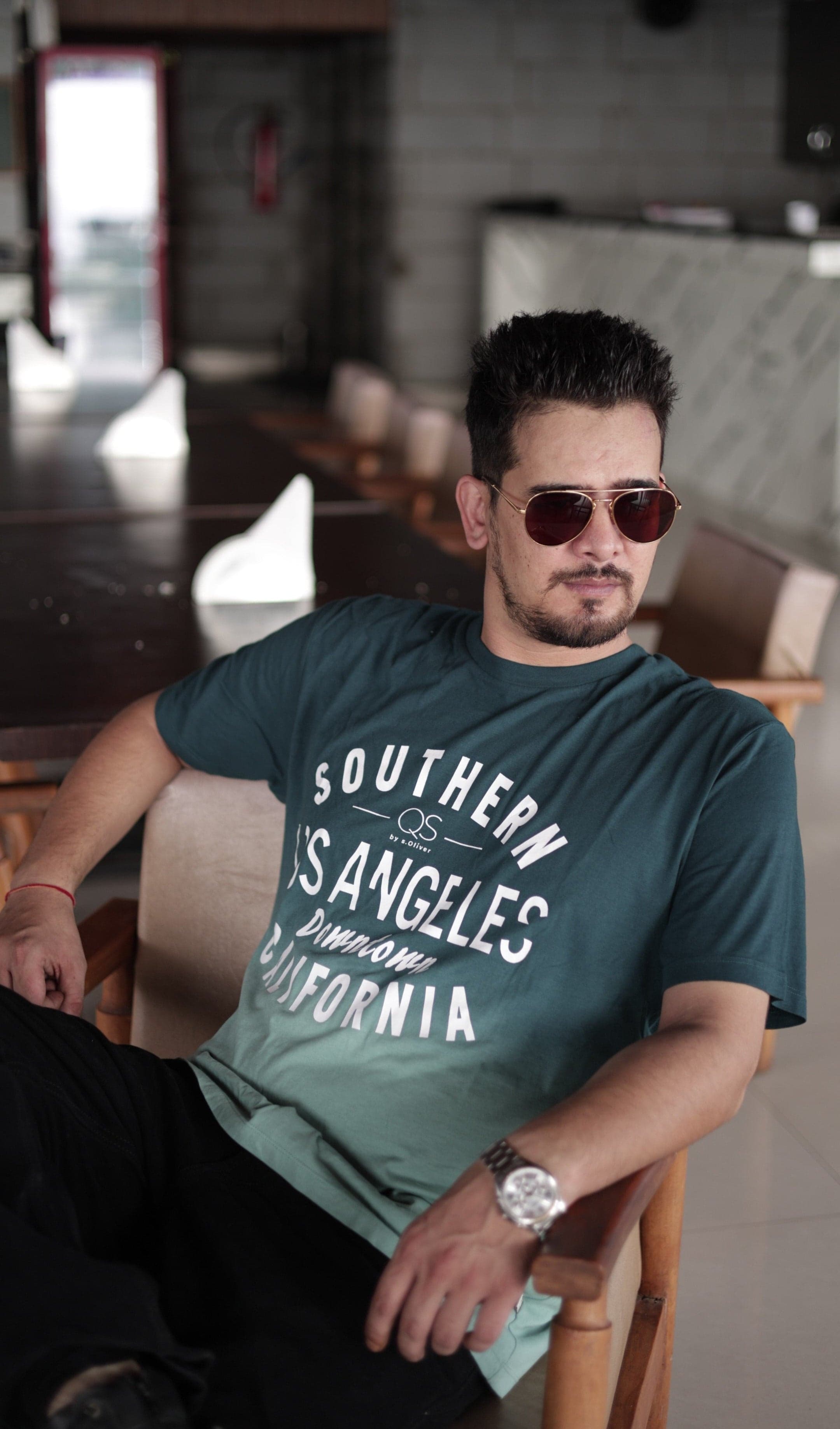 Man wearing a green t-shirt with text, sitting in an indoor setting.