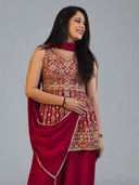 Woman in a red saree with gold embroidery on a stone floor.