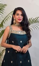 Woman in a dark blue saree with gold patterns standing next to green plants against a light background