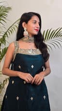 Woman in a dark blue saree with gold patterns standing next to green plants.