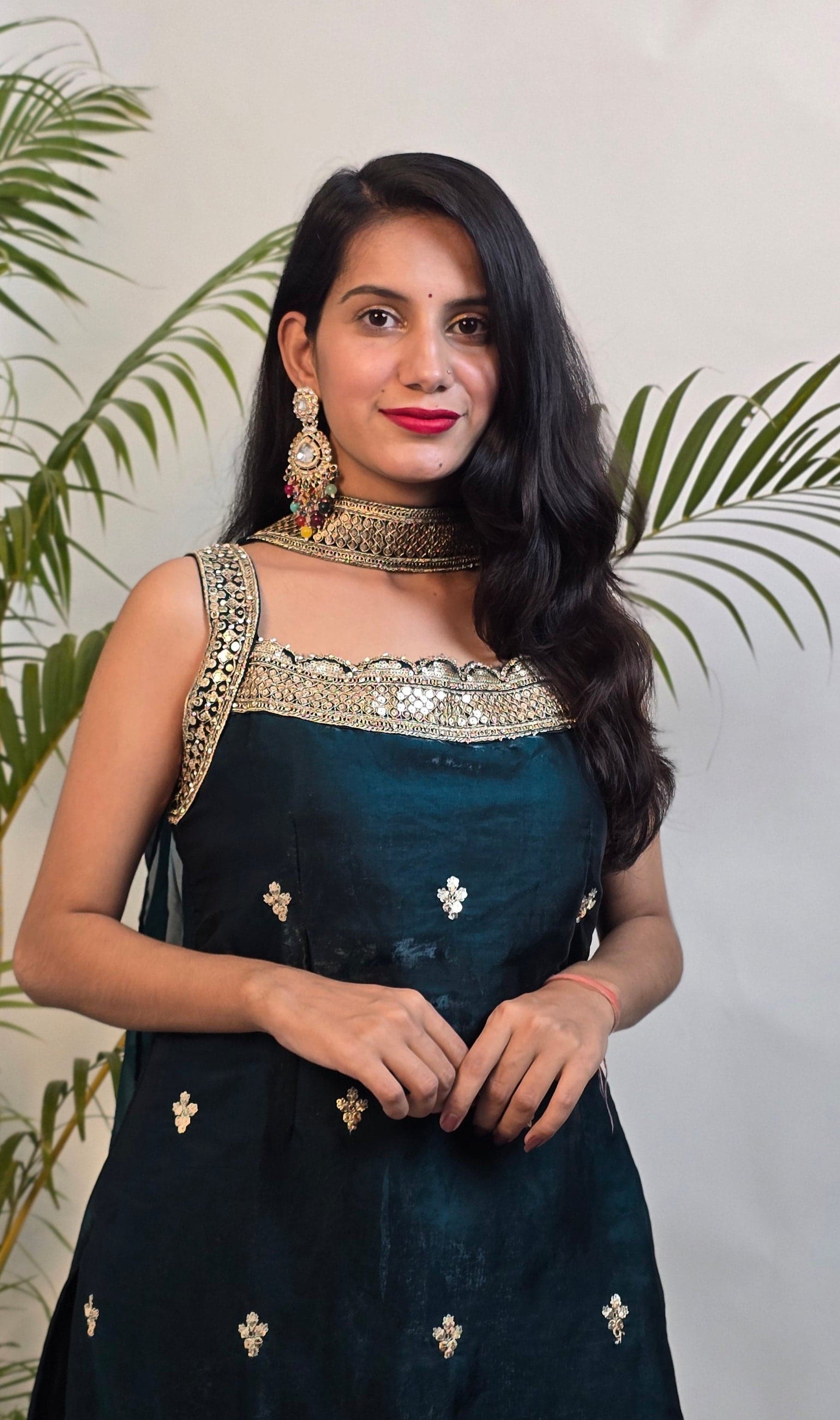 Woman in a dark blue saree with gold patterns standing next to green plants against a light background